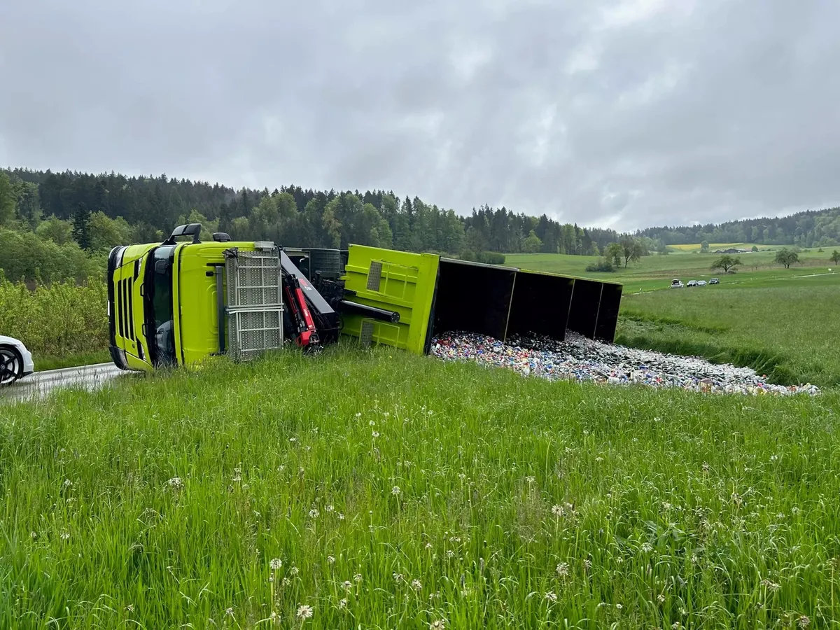 Ein grüner Lastwagen liegt umgekippt neben einer Wiese.